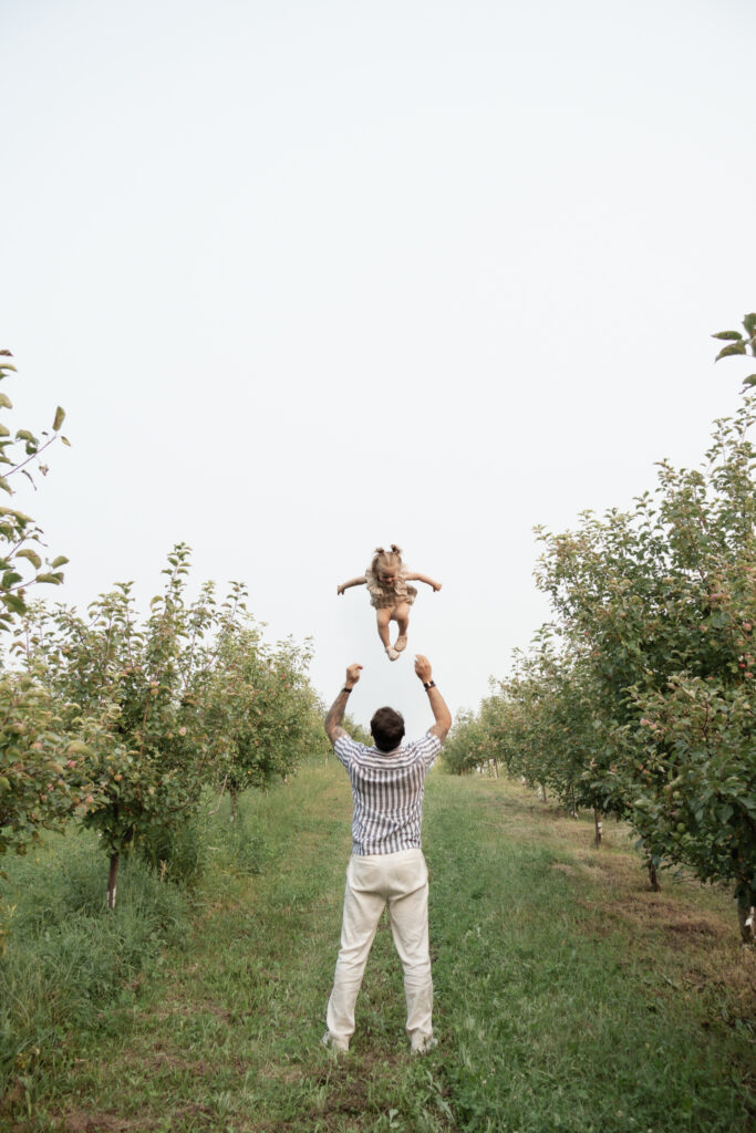 man throwing girl in air in apple orchard