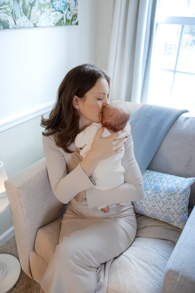 woman holding newborn baby, kissing head while sitting on chair